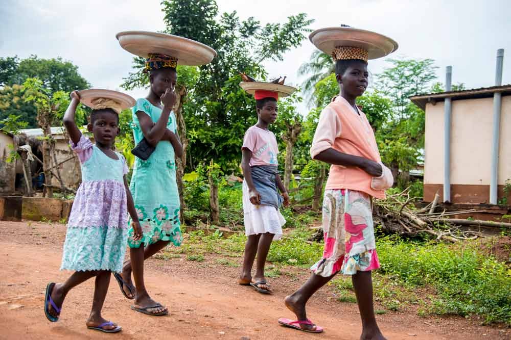 Young women carry baskets on their heads.