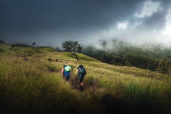 Two people hiking with backpacks with a stormy sky in the background.