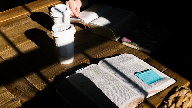 Open Bibles and notes on a wooden table with coffee cups