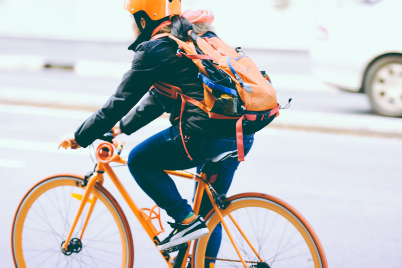 person riding orange bicycle wearing a helmet and backpack