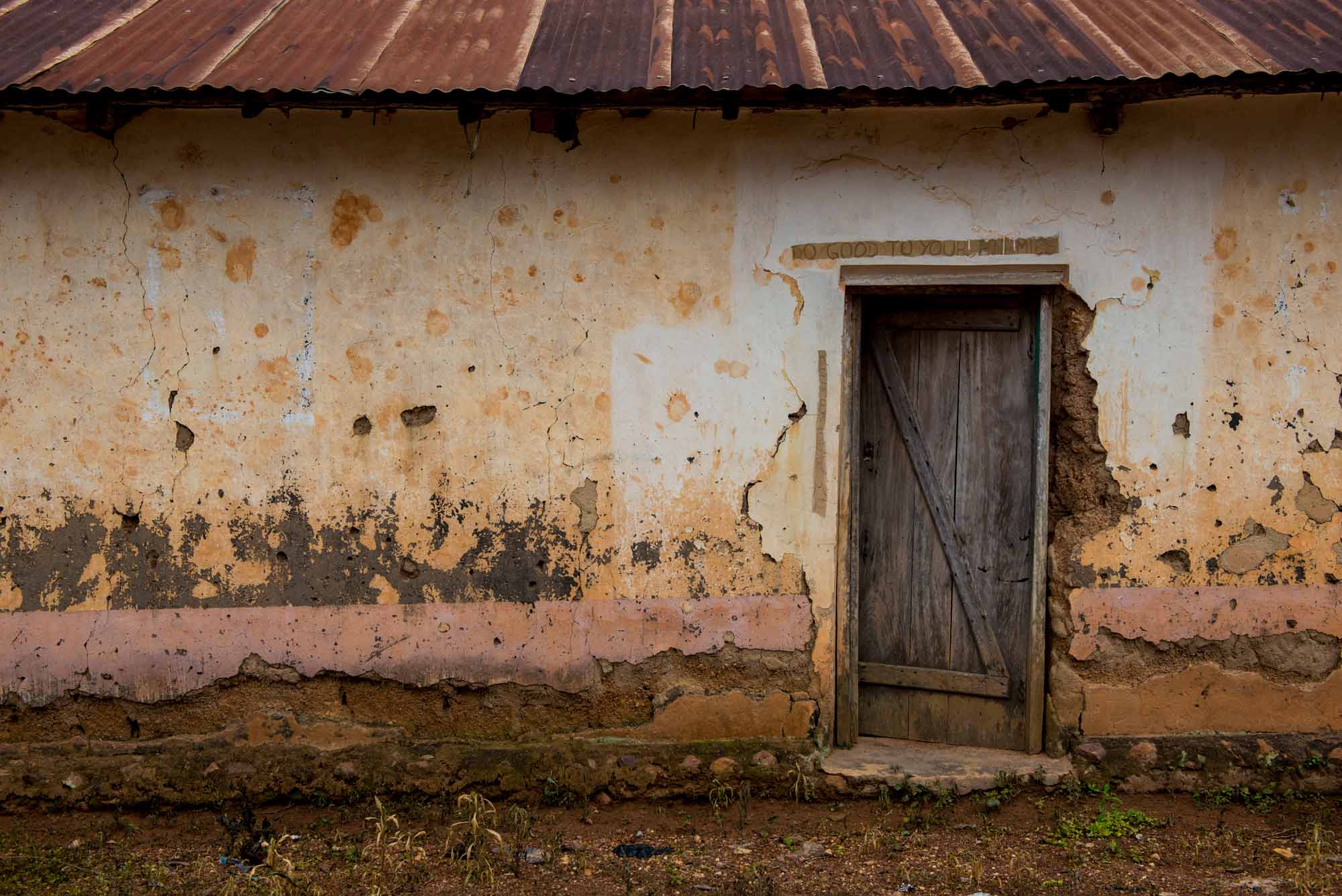 text written above a village house door says 'Do good to your enemies'