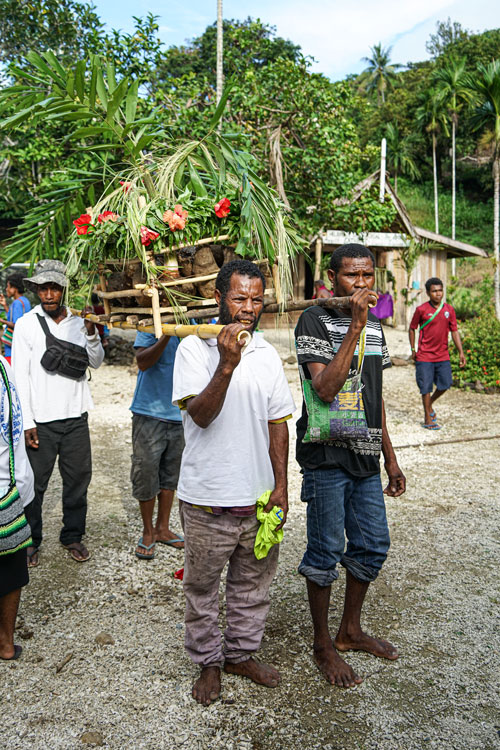 /></figure>
<p>At the church entrance, leaders received the New Testament, ushering it inside for a moving dedication service.</p>
<p>During the service, the representative of the bishop of the United Church in Milne Bay Province prayed for the New Testament and blessed it. The service was accompanied with songs by the various choir groups. Afterward, the celebration continued with joyful dancing and speeches. Members of the United Church translation team even received certificates of appreciation. The day concluded with a celebratory, traditional big meal!</p>
<p>But that wasn’t the only celebration that took place that week.</p>
<h3>Celebrations Across the Island</h3>
<p>Just three days later, on Oct. 15, the Kwato Church of Papua New Guinea hosted a second celebration, welcoming the Saliba New Testament.</p>
<p>The current and former bishop traveled to officially receive the New Testament into the church. At the dedication, they talked about the importance of the Bible for Christian faith and encouraged the believers to read the New Testament in their language. The program continued with speeches, dance and songs from the choir. All the speakers expressed great joy at finally having God’s Word in their language!</p>
<figure class= Four Saliba translators carrying in the replica house that contained the New Testament.