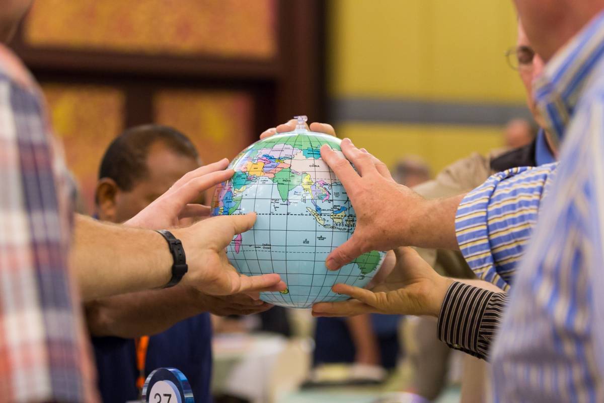 Group of people coming together to hold a globe, symbolizing collaboration of the global Church.