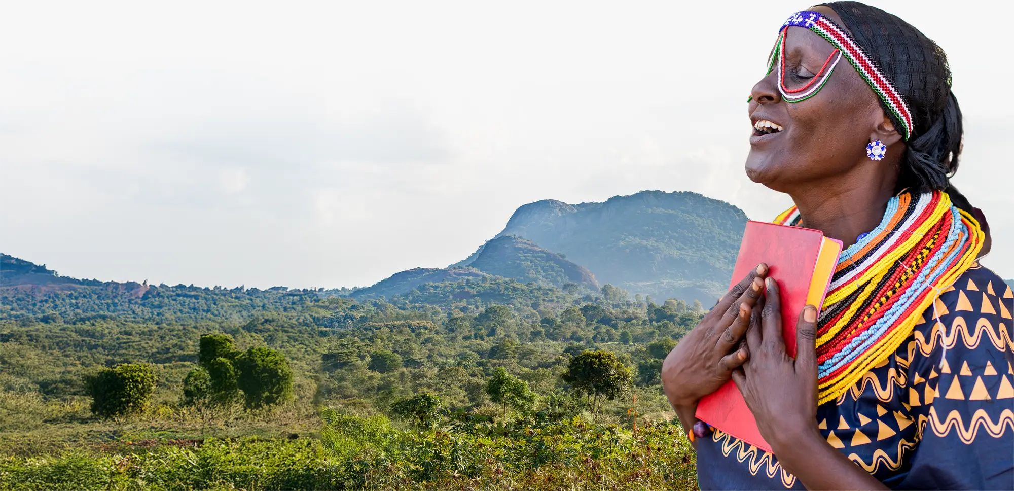 Woman in front of an African landscape clutching a Bible to her heart